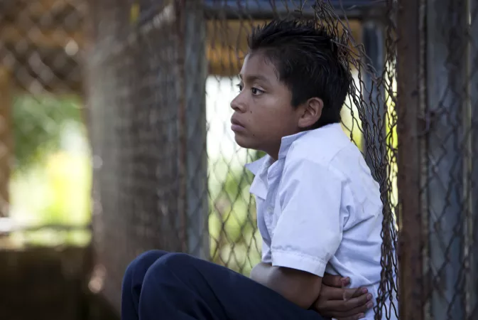 A boy sitting back against a wired fence at school in El Salvador