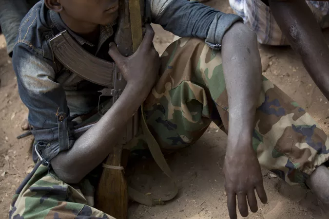 South Sudan. A child sits while holding a gun.