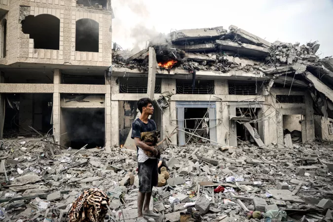 Gaza. A boy stands holding his cat next to the remains of damaged buildings.