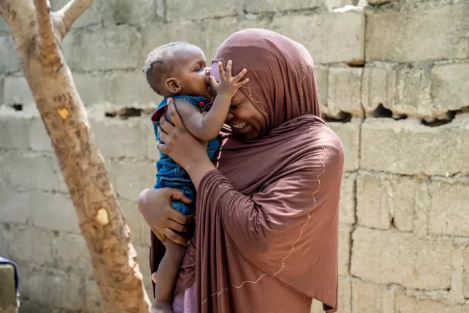 A mother holds her baby, who kisses her on the forehead.