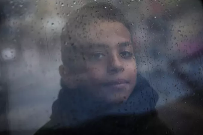 State of Palestine.A boy wearing a scarf looks through a window on a rainy day in the city of Rafah.