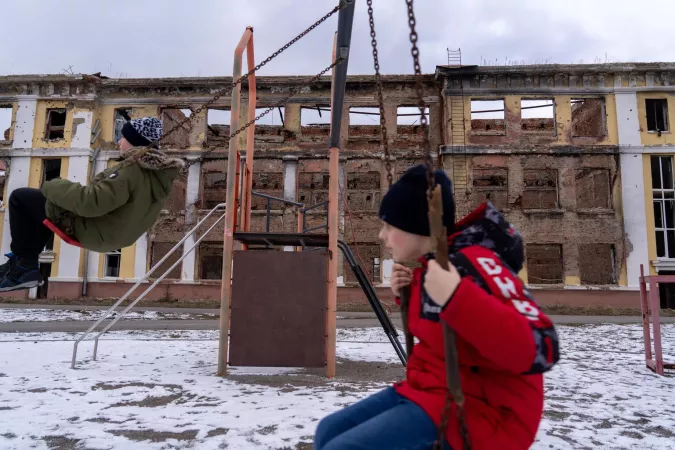 Ukraine. Two boys play on a swing in front of the remains of their school.