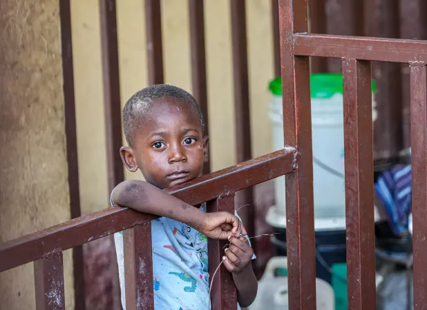 Haiti. A boy stands behind a gate at a site for internally displaced people.