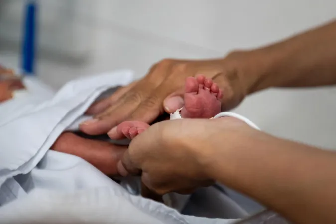 A nurse holds the tiny feet of a newborn in neonatal care at a hospital.