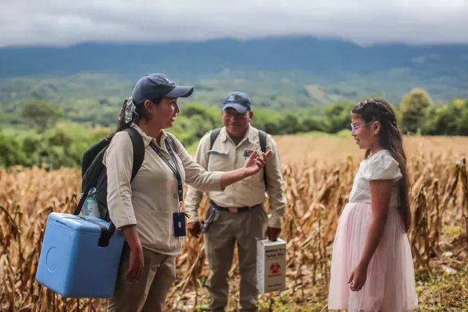 Two healthcare workers carry ice boxes and speak to a child.