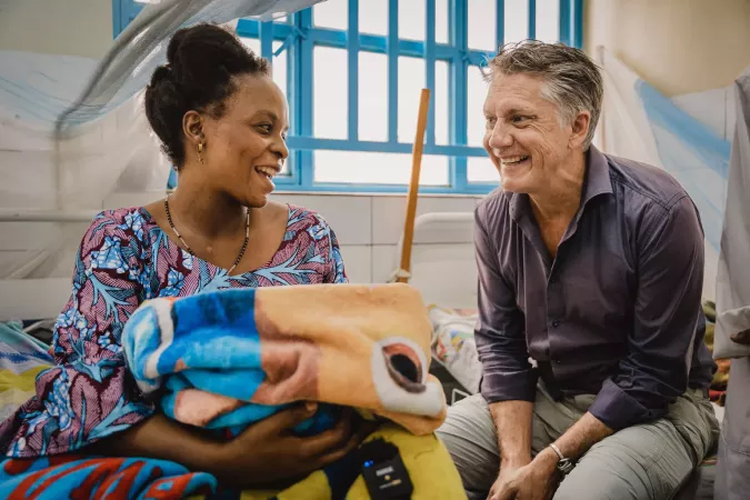 A woman holding her baby in a blanket sits next to a man.
