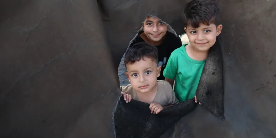 Three children look out from a hole in a tent following the ceasefire announcement in Gaza.