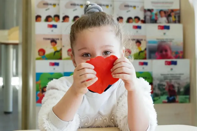 Girl holds red heart in front of her face. 
