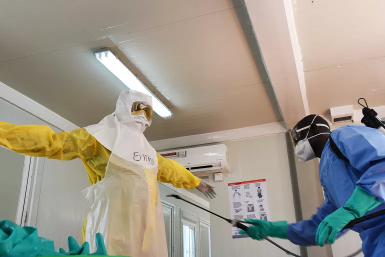 A health worker is doffing the personal protection suit he has been wearing. There are specific protocols for donning and doffing in the context of Ebola to ensure the health worker is not infected.  For every layer of clothes, a sprayer is disinfecting the health worker with a chlorine solution. UNICEF is training frontline health workers on correct infection prevention and control (IPC) as part of the preparedness activities in South Sudan.