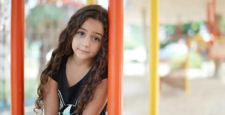 A young girl leans against a post