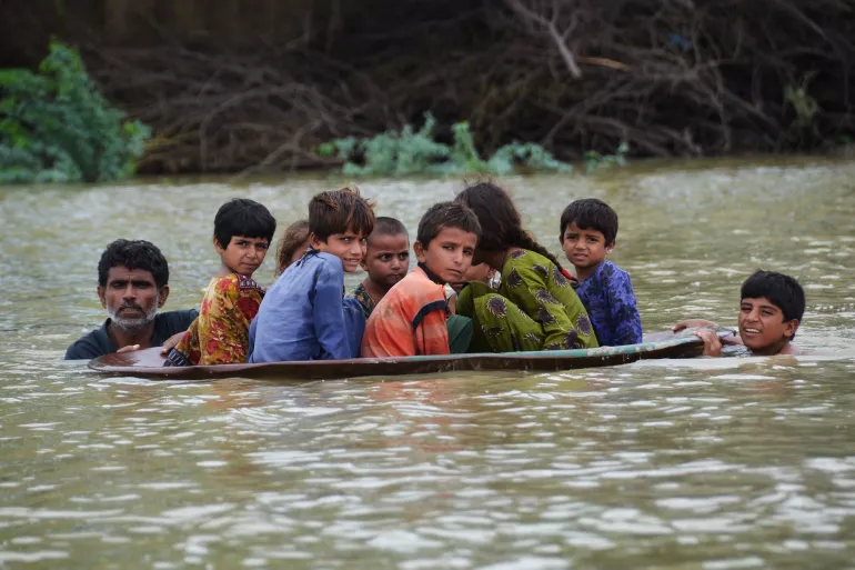 On 26 August 2022, a man (L) and a youth (R) use a satellite dish to move children across a flooded area after heavy monsoon rainfalls in Jaffarabad District, Balochistan Province, Pakistan.