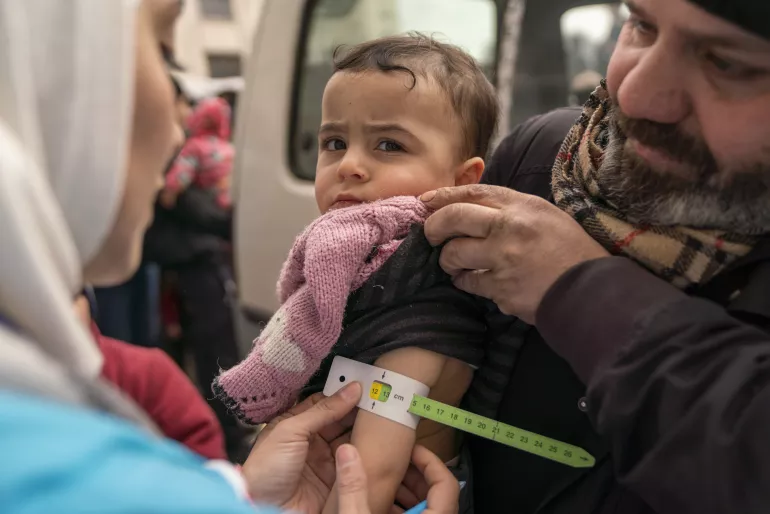 On 10 February 2023, Sondos, two years and eight months, in her father&rsquo;s arms, is screened for malnutrition by a UNICEF-supported mobile health team worker, using a mid-upper arm circumference (MUAC) tape, in the Alsalheen neighbourhood, Aleppo city, north Syria.