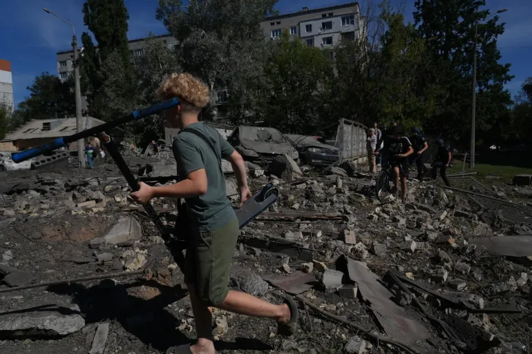 20 August 2026, Kyiv, Ukraine. Children carry a scooter and a bicycle across rubble and debris in Kyiv&rsquo;s Solomianskyi district following a massive overnight attack on the city. Damaged and burned-out vehicles can be seen behind them as residents move through the affected area.