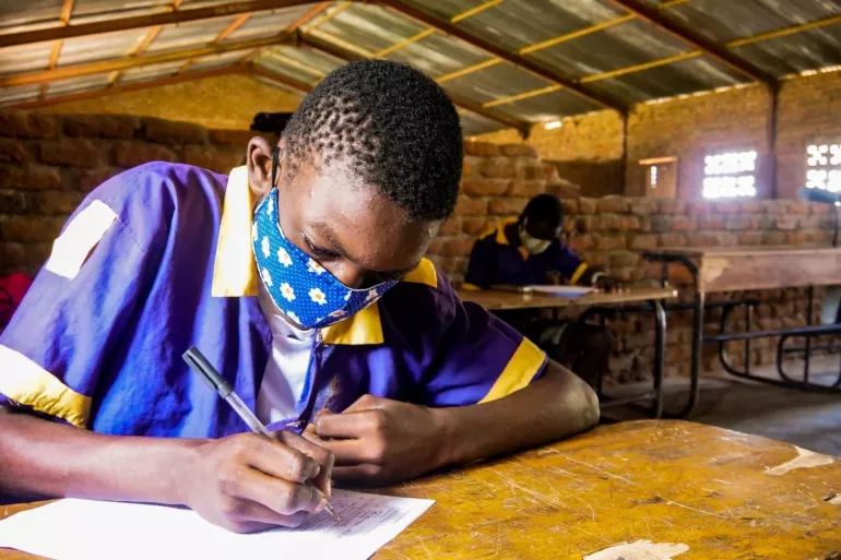 Malawi. A boy writes at a desk in a classroom.