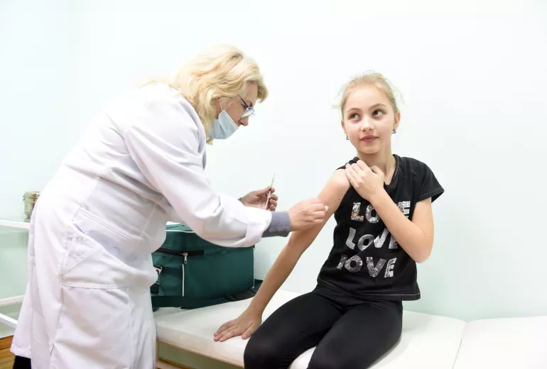 Une infirmiere administre une dose de vaccin a une jeune fille assise.