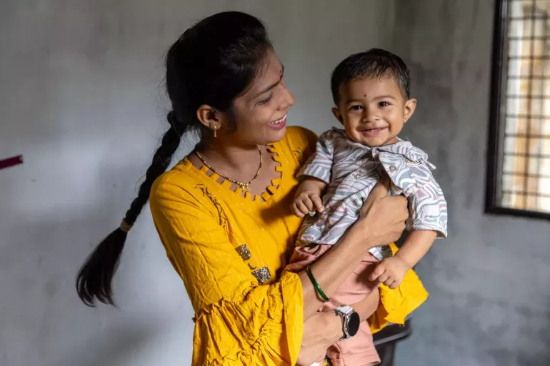 A smiling little boy is held by his mother. 
