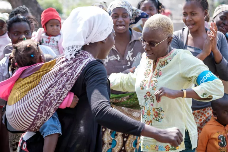 UNICEF Goodwill Ambassador Angelique Kidjo dances with a woman carrying a baby in a sling pouch on her back, during a nutrition education session for mothers in the Madinguine community in Moamba. 