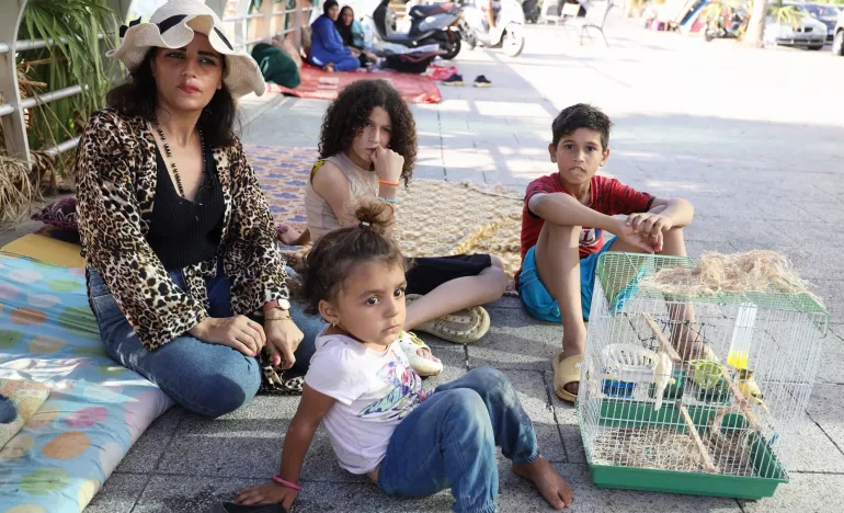 Lebanon. A woman sits on a sidewalk with her family.