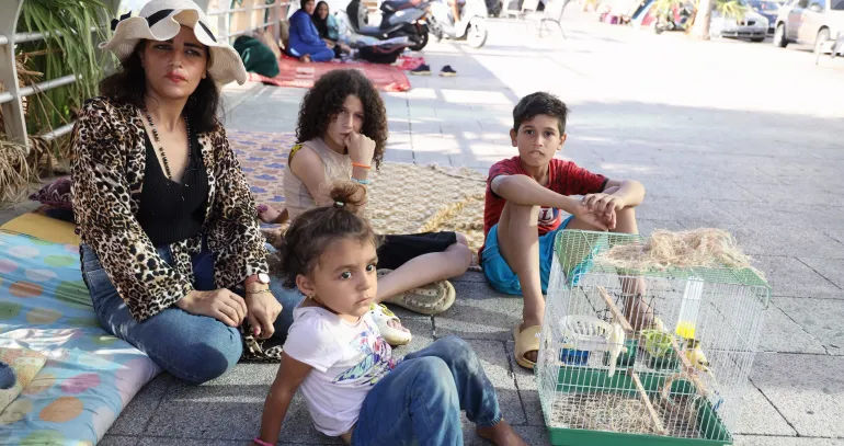 Lebanon. A woman sits on a sidewalk with her family.