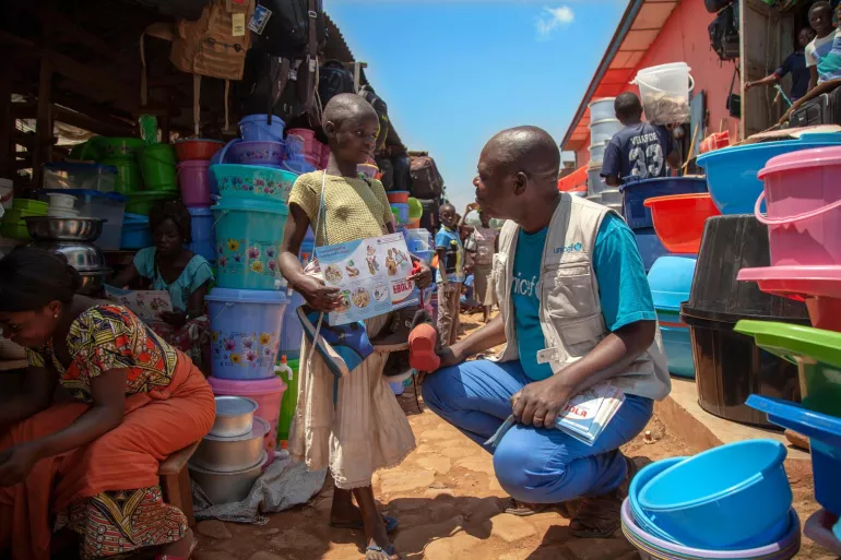 A man crouches next to a girl holding a poster on Ebola, Democratic Republic of Congo