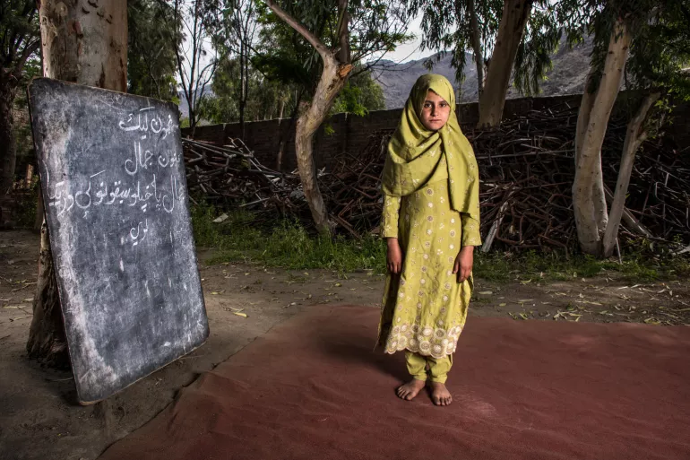 Assiya, 10, stands by a pile of metal debris that was once part of the the Bodyalai girls school, which was destroyed during a bomb blast in 2015, Bodyalai village, Kuz Kunar, Nangarhar province, Afghanistan 9 April 2019. 