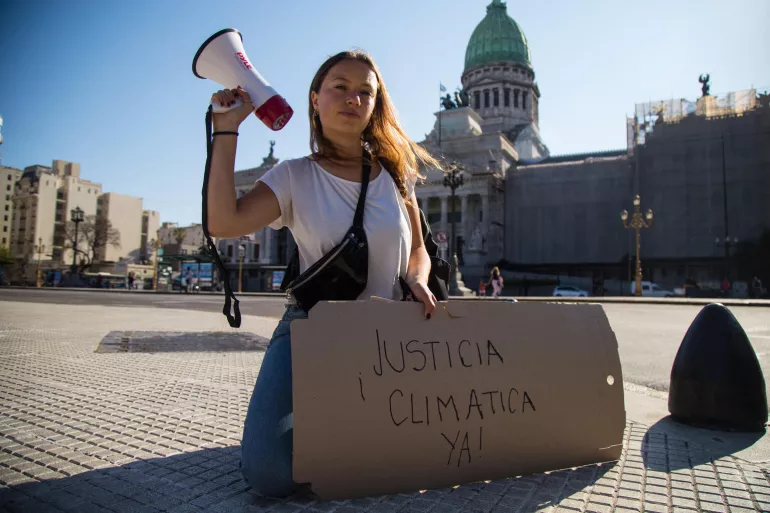 A girl with a loud speaker and a sign that reads "Justice Climatica" protests climate change 