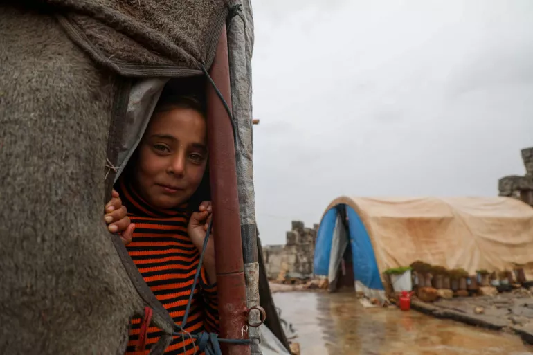 Syria. A girl looks out from a tent at a refugee camp.