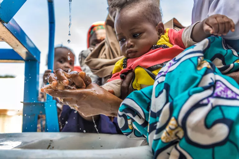 A parent washes the hands of their infant using a tap.