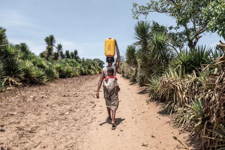 Mother and child walking with water jug.