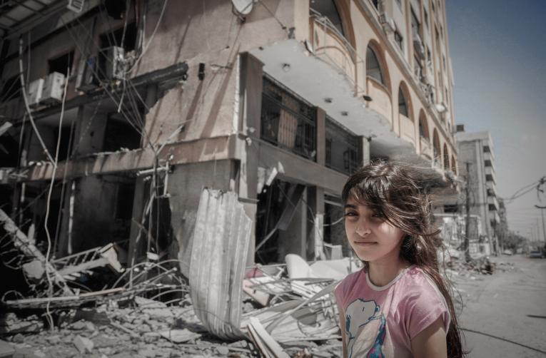 Gaza. A girl stands next to a damaged building.