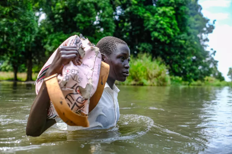 A child wades through water carrying bag of belongings.
