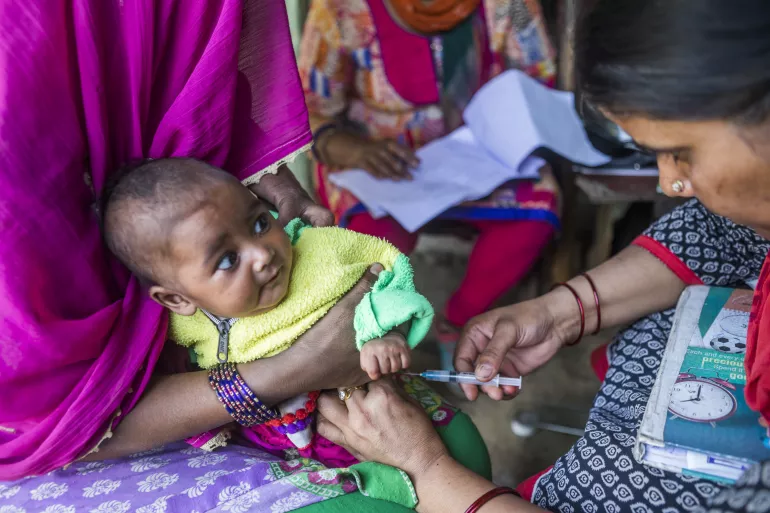 A small, colorfully -dressed baby gets a vaccine shot.
