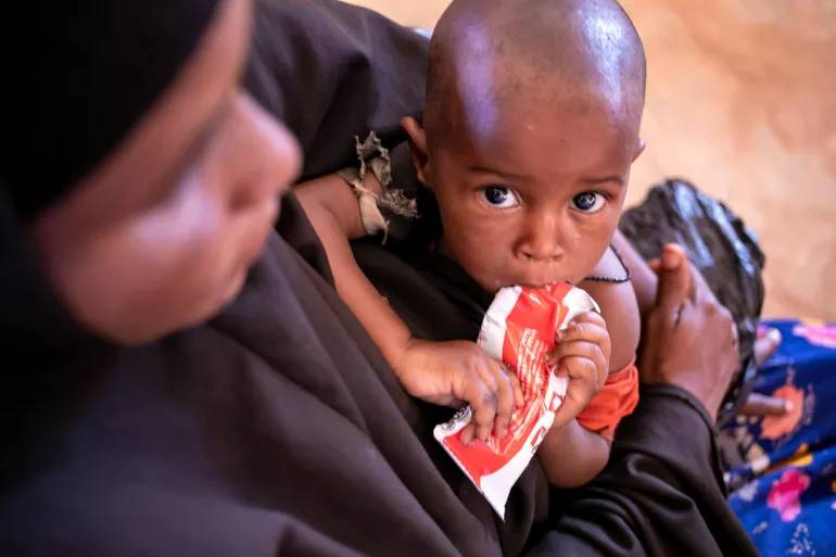 Somalia. A child is held by his mother as he feeds on a sachet of ready-to-use therapeutic food.