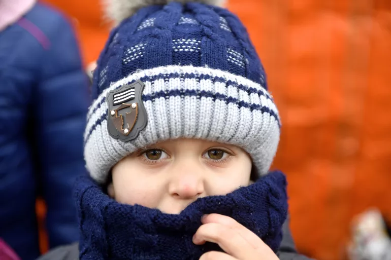 Ukraine. A small child wearing a hat and jacket looks at the camera.