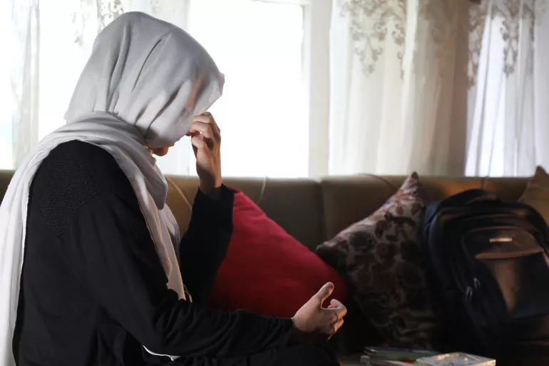 Une fille est assise pr&egrave;s d'une fen&ecirc;tre. Elle se cache le visage avec sa main. 