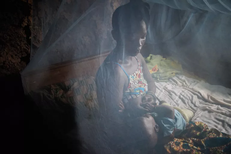 A woman and her child sit on a bed under a mosquito net, Sierra Leone