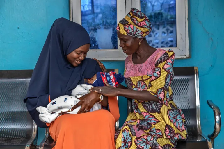 A young mother receives support from a community elder while breastfeeding her baby. 