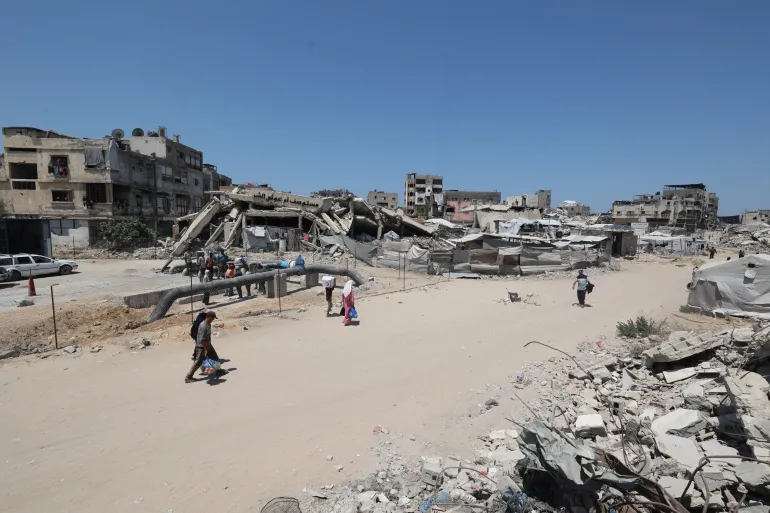 People walk along a road cleared between the rubble of destroyed buildings.