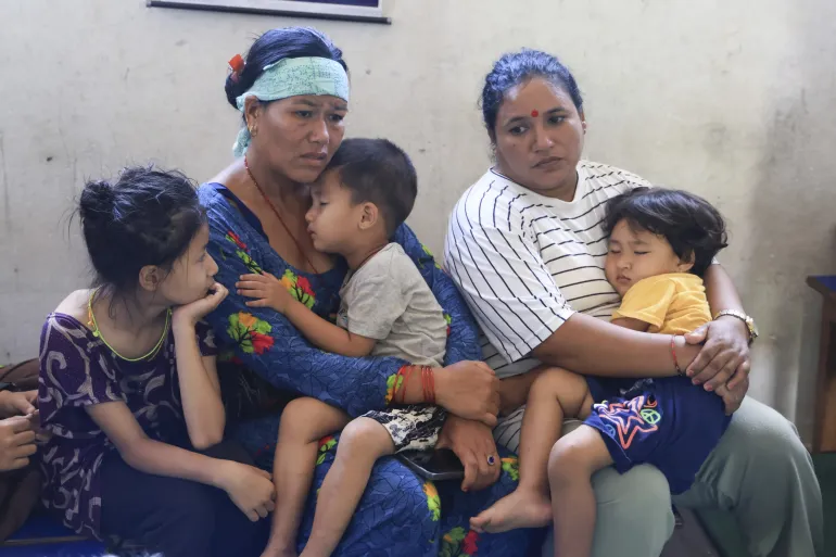 Two women and three children sit, exhausted, in a school room.