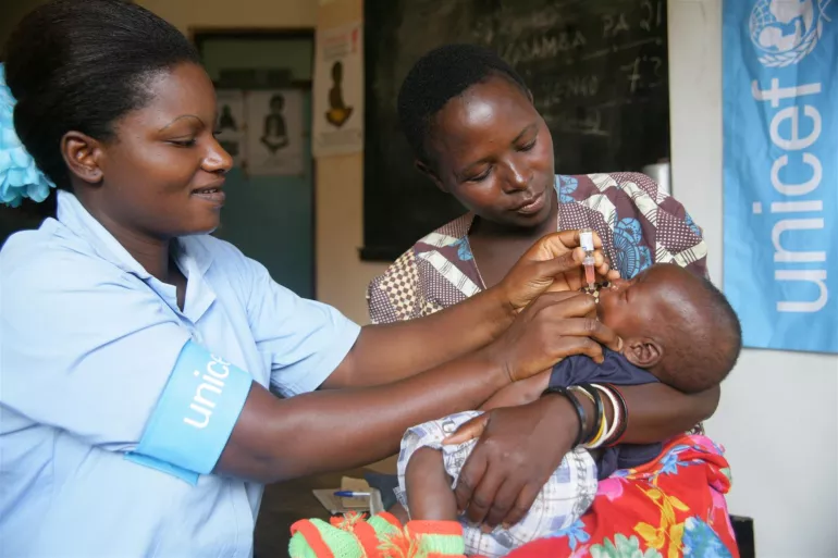 A health worker gives polio vaccine to an infant held by her mother