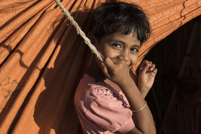 On 27 November 2019, a girl smiles next to her home in the Balukhali refugee camp in Cox&rsquo;s Bazar, Bangladesh.