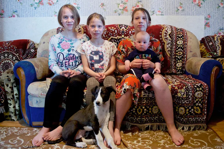Yana, 12, Lyubov, 10, Arina, 13 and Daniil, 7 months, sit in the living room of their small rented house in Nur-Sultan, Kazakhstan.