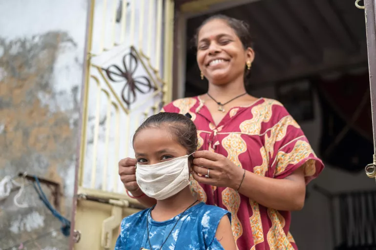 Una madre le pone una mascarilla a su hija. India.
