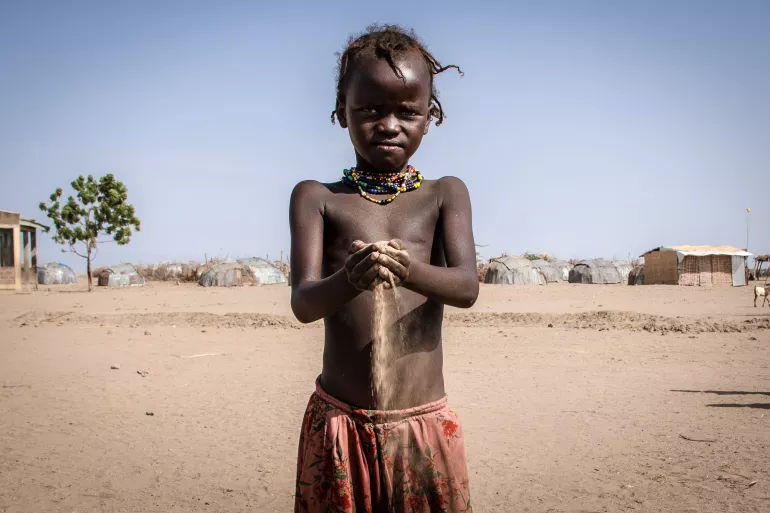 a child stands with sand running through his fingers. he is in an arid landscape.