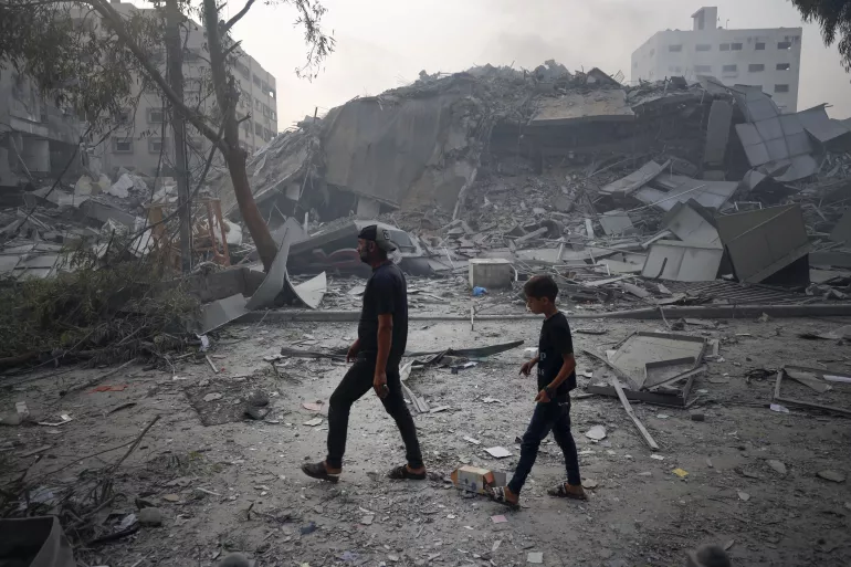 A child and his father walk past the rubble of buildings.