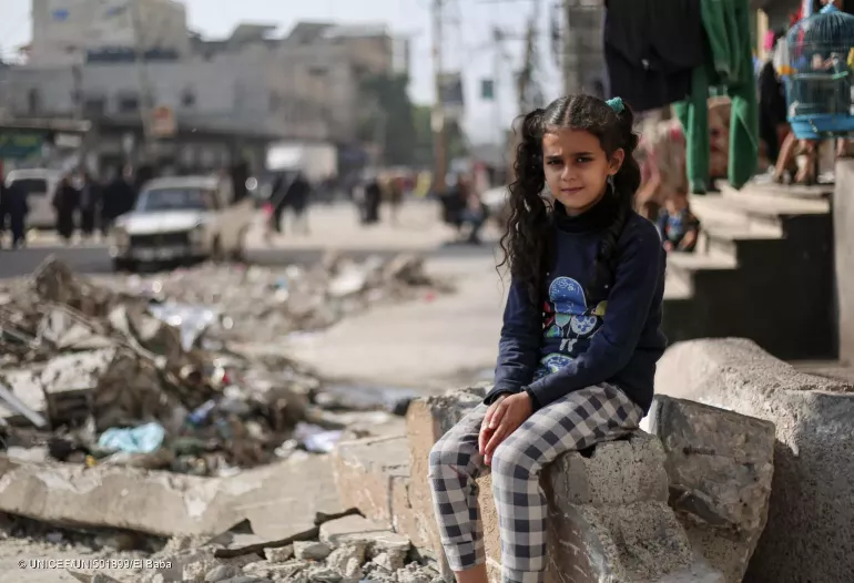 Girl is sits on the rubble of a house.