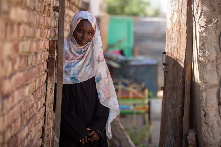 A girl stands by her home