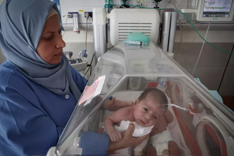 A healthcare worker holds a baby inside an incubator.
