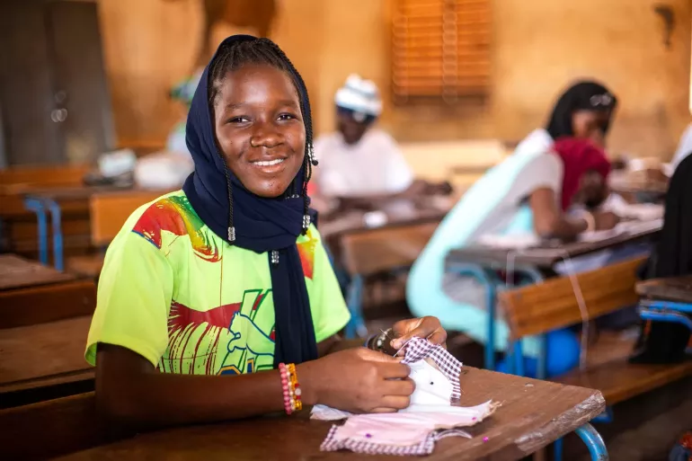 Girl sits at a desk making reusable pads in a school. 