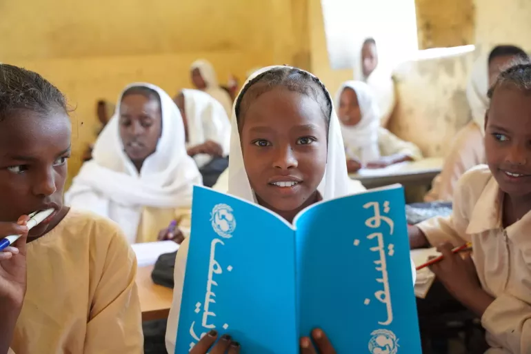Student looks at the camera as she opens her blue notebook. 